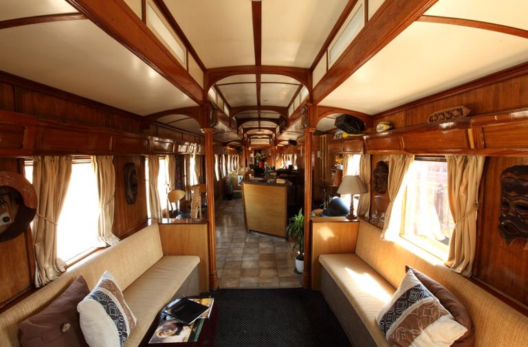 Wagon salon du train Shongololo Express avec boiseries luxueuses, sofas beiges et décoration africaine