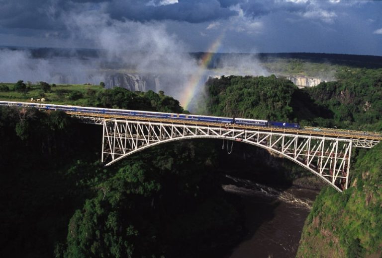 Blue Train traversant le pont Victoria Falls avec arc-en-ciel et chutes en arrière-plan, Afrique australe