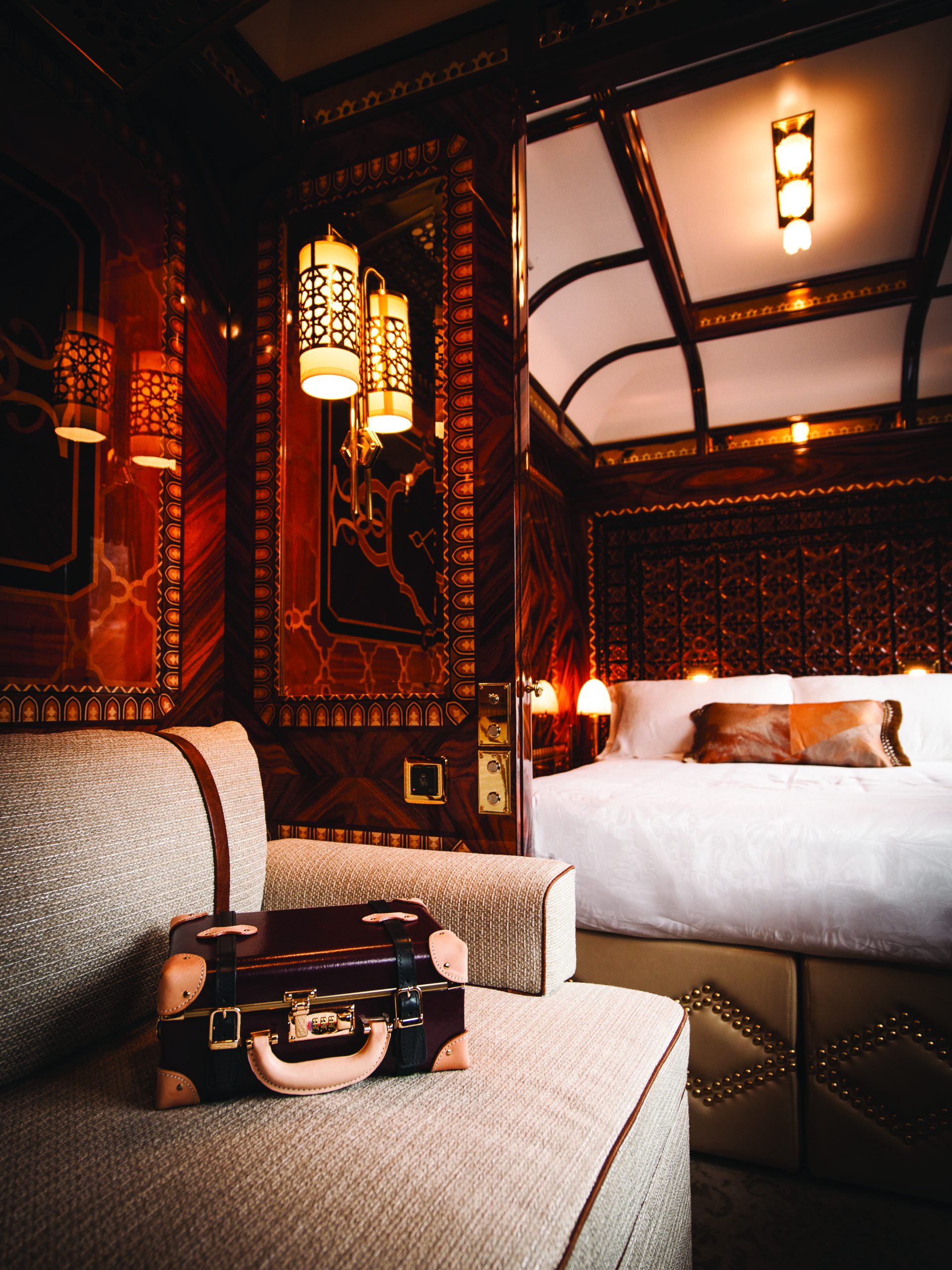 Intérieur luxueux Grand Suite Venice Simplon Orient Express avec lit double, boiseries Art Déco et valise vintage