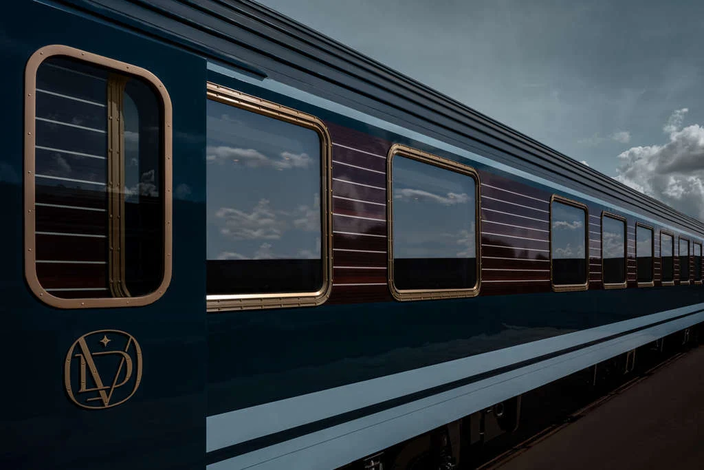 Voiture de train de luxe bleu nuit avec fenêtres encadrées de laiton doré et logo élégant sur le quai