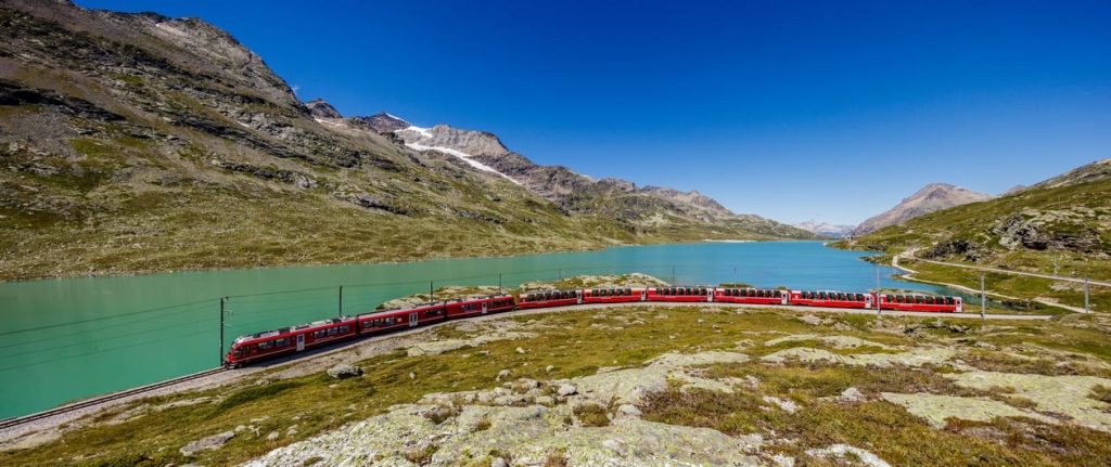 Bernina Express rouge longeant le Lago Bianco turquoise dans les Alpes suisses sous un ciel bleu