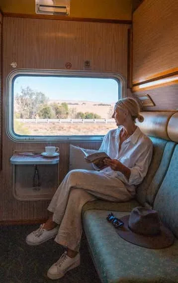 Voyageuse lisant dans une cabine Gold du train australien avec vue sur les plaines arides de l'Outback