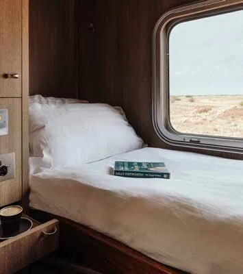 Cabine Gold Single du train Indian Pacific avec vue sur la plaine du Nullarbor - literie blanche et livre posé