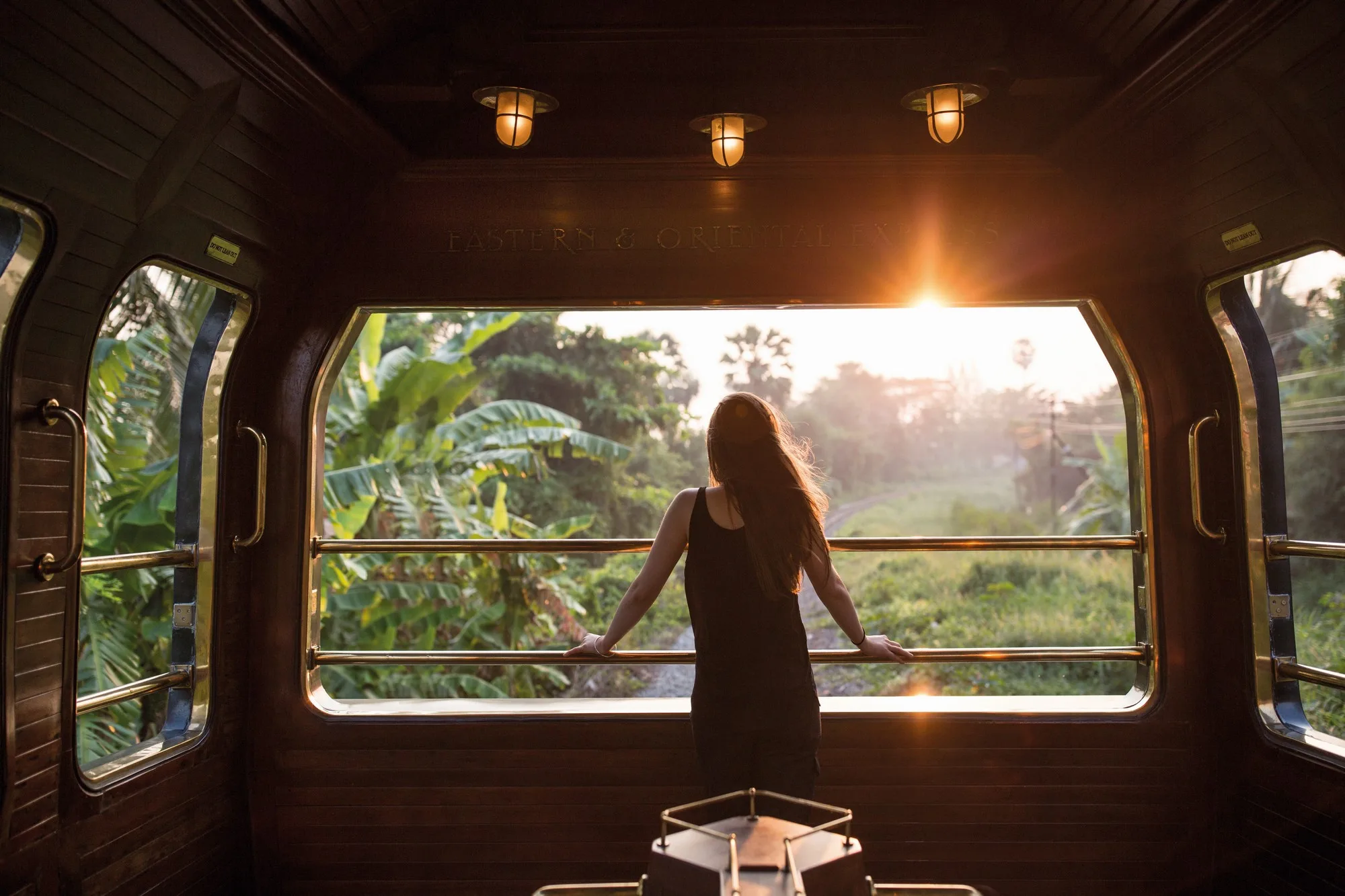 Voyageuse admirant le coucher de soleil tropical depuis la voiture d'observation de l'Eastern Oriental Express