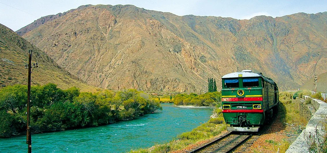 Train longeant une rivière turquoise dans les montagnes du Kirghizstan