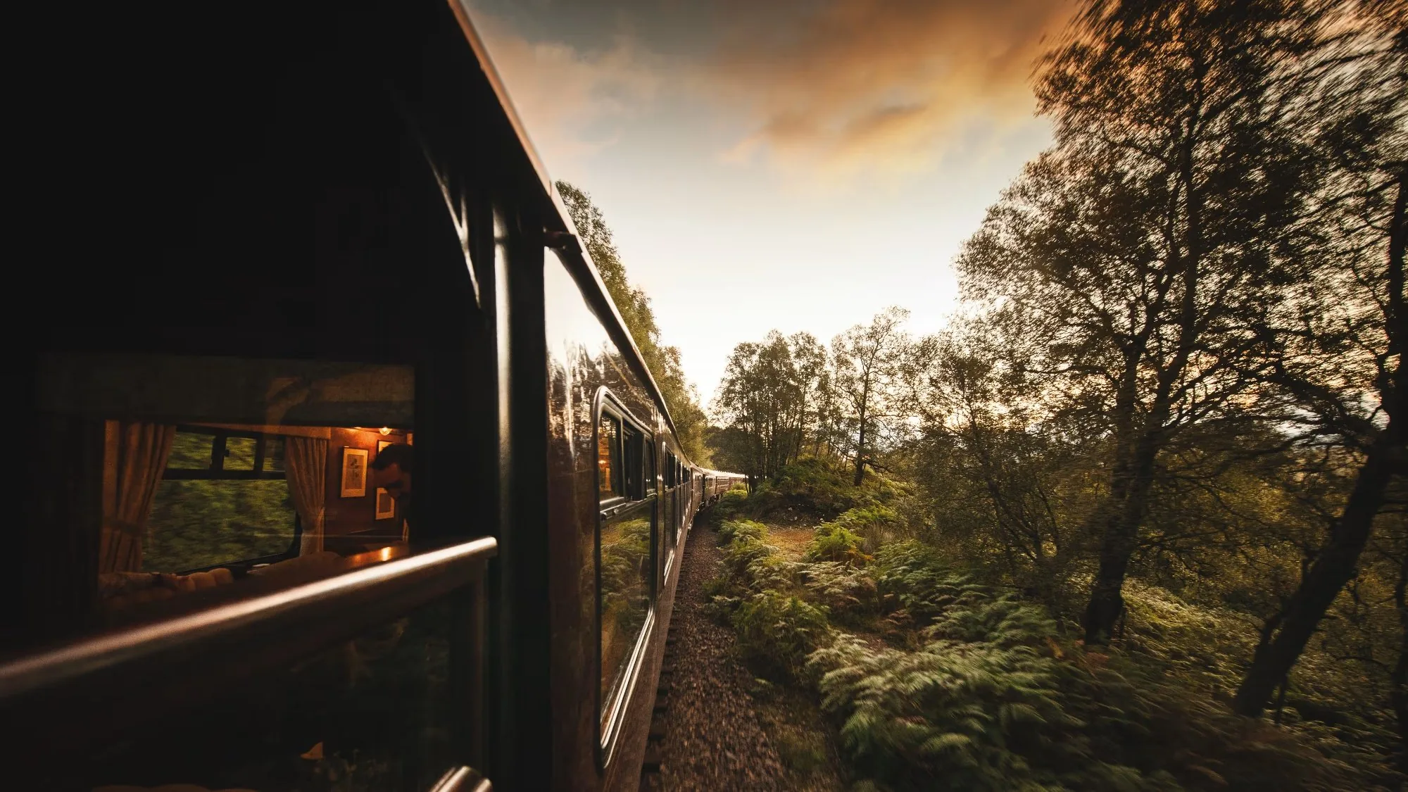Belmond Royal Scotsman traversant la forêt des Highlands écossais au coucher du soleil — reflets dans les fenêtres