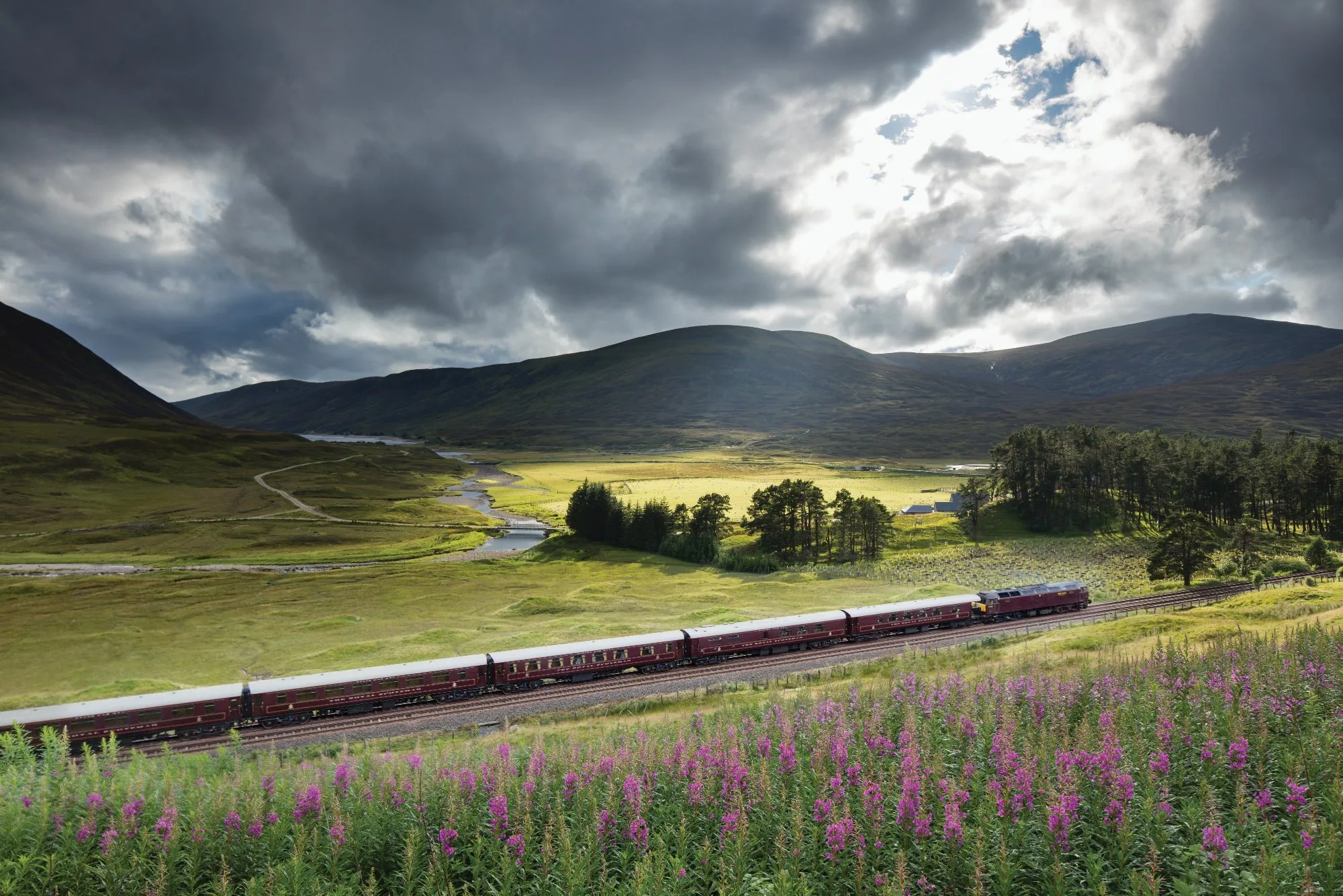 Belmond Royal Scotsman dans les Highlands écossais — train bordeaux traversant la bruyère et les montagnes sous un ciel dramatique