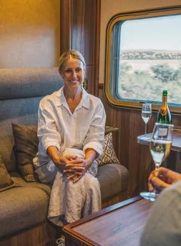 Passagère dans le salon d'un train de luxe australien Journey Beyond avec champagne et vue sur l'Outback