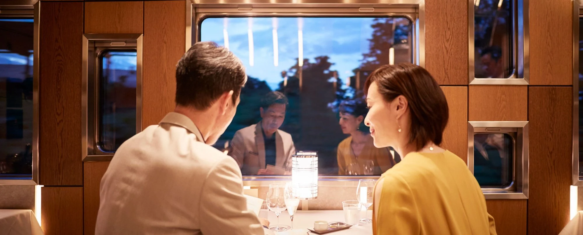 Couple dînant à bord du Train Suite Shiki-Shima la nuit — restaurant gastronomique avec vue sur le Japon nocturne