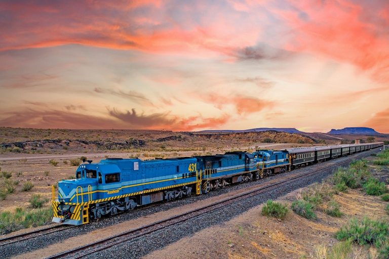 African Explorer train de luxe bleu traversant le désert africain au coucher de soleil