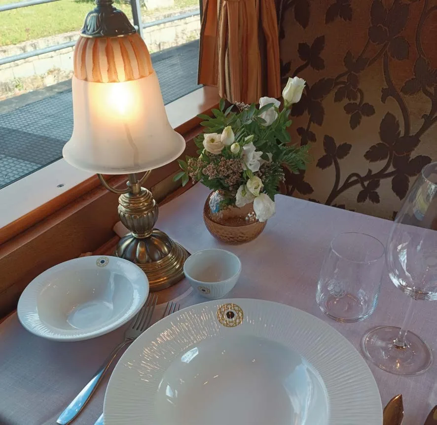 Table dressée à bord du Transcantábrico Gran Lujo avec vaisselle au logo Renfe Trenes Turísticos de Lujo et lampe Art Déco